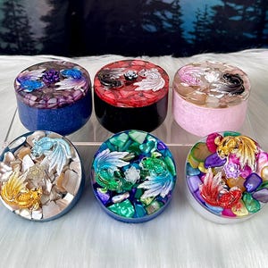 May include: Six round trinket boxes with different coloured resin tops and various designs of fish and flowers. The boxes are all about 7.5 cm in diameter.