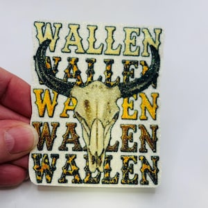 May include: A rectangular sticker with the word "WALLEN" in a repeating pattern. The sticker features a bull skull with black horns and a tan skull. The text is in a gold and leopard print pattern.