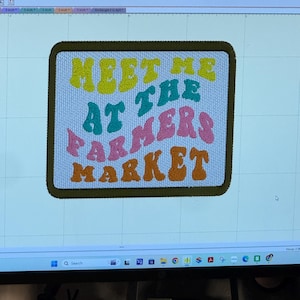 May include: A rectangular patch with the text "MEET ME AT THE FARMERS MARKET" in yellow, teal, pink, and orange bubble letters. The patch has a light blue background and a dark green border.