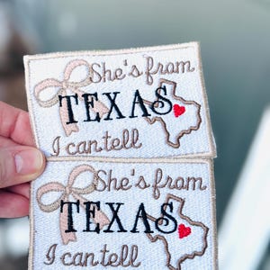 May include: Two embroidered patches with the text "She's from TEXAS I can tell". The patches feature a Texas outline with a red heart, a bow, and a light blue background.