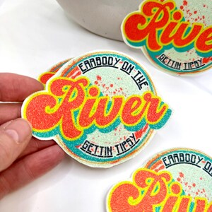 May include: A collection of colorful stickers with a retro design. The stickers feature the words "Earrbody on the River" and "Gettin Tipsy" in a vibrant red and yellow font, with a teal and white background. The stickers are round with a wavy border.