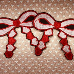 May include: Two white and red embroidered fabric bows with a chain of alternating red and white hearts.
