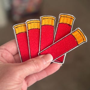 May include: Five red and orange shotgun shell patches. The patches are embroidered with white stitching.