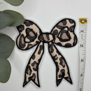May include: A brown and black leopard print bow with a black outline. The bow is approximately 3 inches wide.