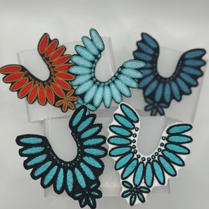May include: Five embroidered patches in the shape of a collar. The patches are in various shades of blue, teal, and red. The patches are all the same size and shape.