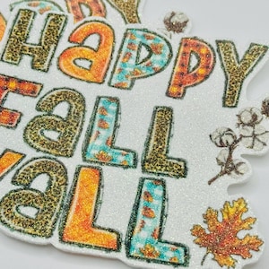May include: A glittery white sign with the words "Happy Fall Y'all" in orange, teal, and leopard print lettering. The sign is decorated with cotton and a fall leaf.