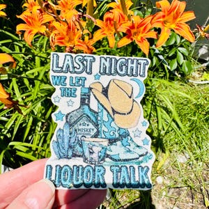 May include: A glittery sticker with the text "LAST NIGHT WE LET THE LIQUOR TALK." The design includes a cowboy hat, boots, a whiskey bottle, and a shot glass, all in shades of blue and tan. Stars and a crescent moon are also featured.