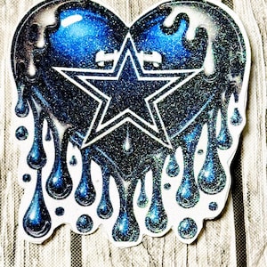 May include: A heart-shaped sticker with a dripping design. The heart is blue with a glittery texture and a white outline. A white star is in the center. The dripping effect has blue and silver accents.