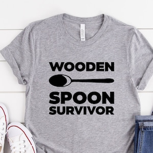 May include: A gray t-shirt with a black graphic that says "Wooden Spoon Survivor" and a black silhouette of a wooden spoon.