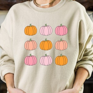 May include: A beige sweatshirt with a graphic print of nine pastel pink and orange pumpkins.