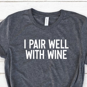 Pu&ograve; includere: Una maglietta grigia melange con il testo "I pair well with wine" in lettere bianche.