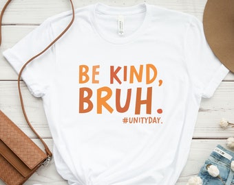 May include: White t-shirt with the text "Be Kind, Bruh." in orange and red lettering. The text "#UnityDay." is printed in black below the main text.