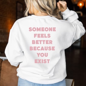 May include: White sweatshirt with the text "Someone feels better because you exist" printed in pink on the back.