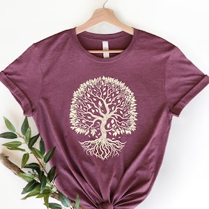 May include: A maroon t-shirt with a yellow tree of life design. The tree has a thick trunk and many branches with leaves. The roots of the tree are visible.