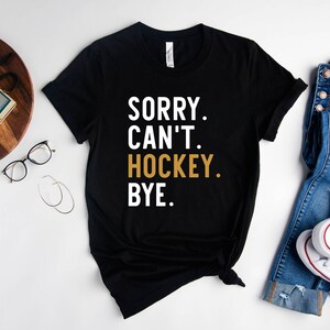 May include: Black t-shirt with the text "SORRY. CAN'T. HOCKEY. BYE." in white and gold lettering.