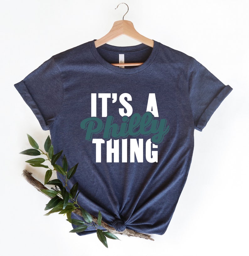 May include: A navy blue t-shirt with white text that reads "It's a Philly Thing". The word "Philly" is in a green font.