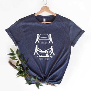 May include: A navy blue t-shirt with a white graphic of two stick figures carrying a couch, labeled "FRIEND." Below that, two stick figures are carrying another stick figure, labeled "BEST FRIEND."