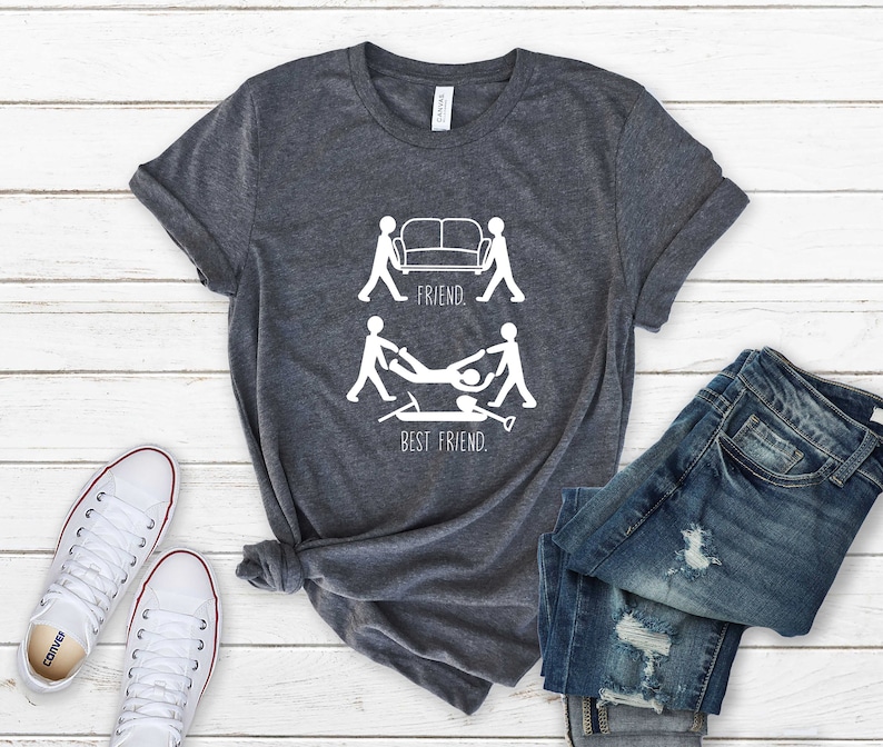 May include: A dark gray t-shirt with a white graphic of two stick figures carrying a couch, labeled "Friend." Below that, two stick figures are carrying a person on a shovel, labeled "Best Friend."
