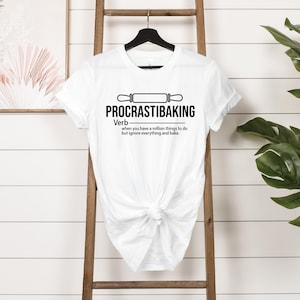 May include: White t-shirt with a black graphic that says "PROCRASTIBAKING" and defines it as a verb: "when you have a million things to do but ignore everything and bake."