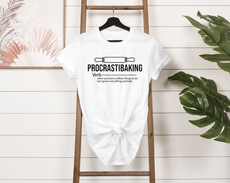 May include: White t-shirt with a black graphic that says "PROCRASTIBAKING" and defines it as a verb: "when you have a million things to do but ignore everything and bake."