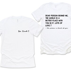 May include: Two white t-shirts with a message on each. The front shirt says "Be Kind" with a heart symbol. The back shirt says "Dear person behind me, the world is a better place with you in it. Lots of love." and is signed "the person in front of you".
