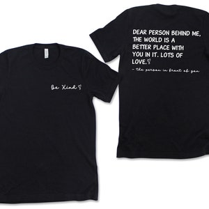 May include: Two black t-shirts with white text. The front shirt says "Be Kind" with a heart symbol. The back shirt says "Dear person behind me, the world is a better place with you in it. Lots of love. - the person in front of you".