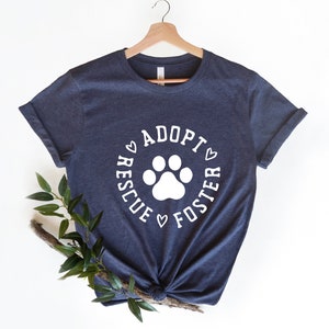 May include: A dark blue t-shirt with a white paw print and the text "Adopt, Rescue, Foster" in a circle around the paw print.