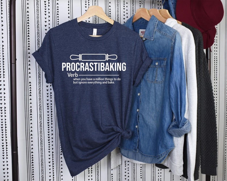May include: A navy blue t-shirt with white text that reads "PROCRASTIBAKING Verb when you have a million things to do but ignore everything and bake."
