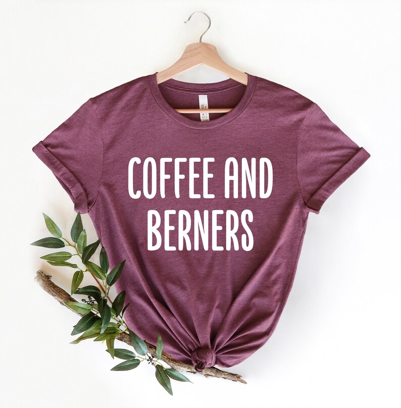 Op de afbeelding: Een maroon t-shirt met de tekst "COFFEE AND BERNERS" in witte letters.