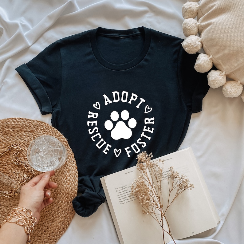 May include: Black t-shirt with a white paw print and the text "Adopt Rescue Foster" in a circle around the paw print.