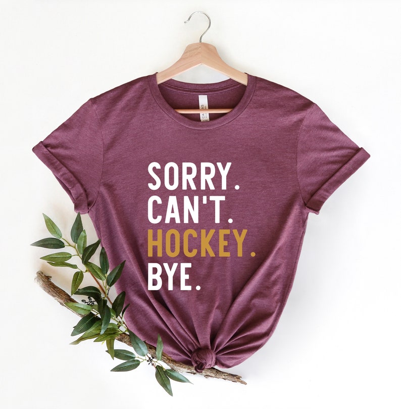 May include: A maroon t-shirt with the text "SORRY. CAN'T. HOCKEY. BYE." in white and gold lettering.