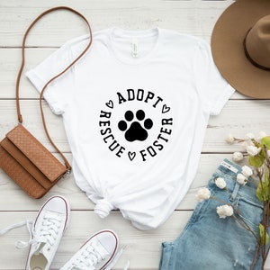 May include: White t-shirt with a black paw print and the text "Adopt Rescue Foster" in a circle around the paw print.