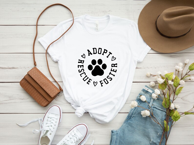 May include: White t-shirt with a black paw print and the text "Adopt Rescue Foster" in a circle around the paw print.