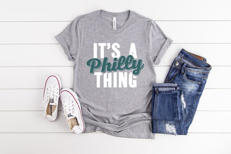 May include: A grey t-shirt with the text "It's a Philly Thing" in white letters with a green and white graphic of the word "Philly".