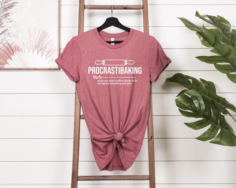 May include: A maroon t-shirt with a white graphic that says "PROCRASTIBAKING" and defines it as a verb: "when you have a million things to do but ignore everything and bake".