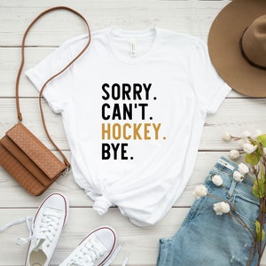 May include: White t-shirt with black text that reads "Sorry. Can't. Hockey. Bye."