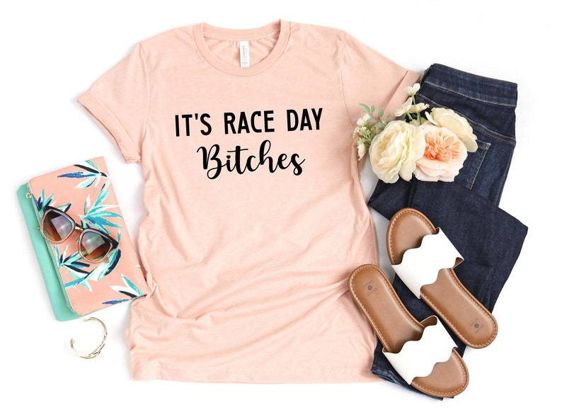 Może przedstawiać: Jasnor&oacute;żowy t-shirt z nadrukiem "It's Race Day Bitches" w kolorze czarnym.