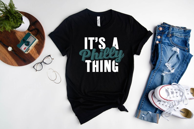 May include: Black t-shirt with white text that reads "It's a Philly Thing" in a green font.