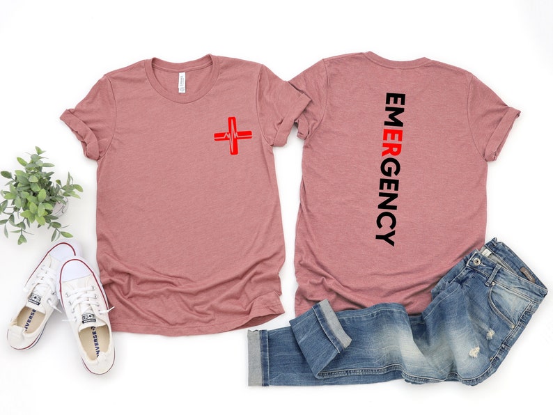 May include: A pink t-shirt with a red medical cross and a heartbeat graphic on the front. The back of the shirt says "EMERGENCY" in black text.