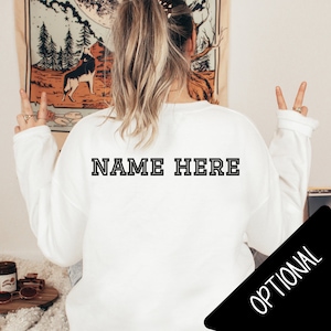 May include: White sweatshirt with black text that says "NAME HERE" on the back. The text is in a bold, blocky font.