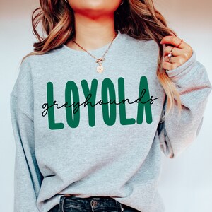 Pode incluir: Uma camisa de moletom cinza com o texto "LOYOLA" em letras verdes e "greyhounds" em escrita cursiva preta abaixo.
