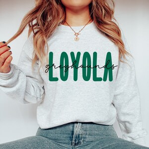 Pode incluir: Uma camisa de moletom cinza com o texto "LOYOLA" em letras verdes e "greyhounds" em escrita cursiva preta.