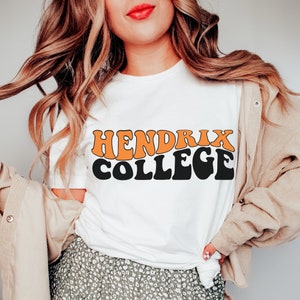 May include: White t-shirt with the text "Hendrix College" in black and orange letters. The letters are in a retro style font.