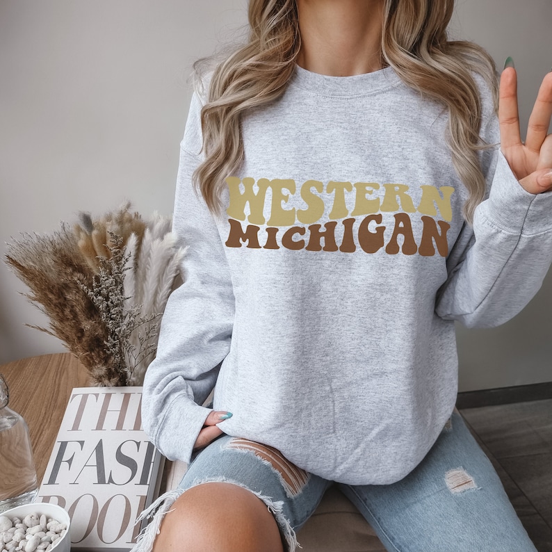May include: A gray sweatshirt with the text "WESTERN MICHIGAN" in brown and beige letters. The letters are in a retro, wavy font.