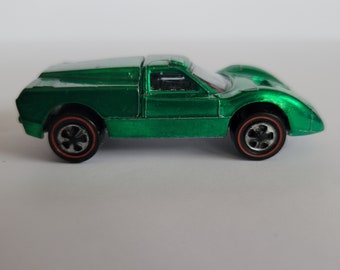 May include: A green die-cast toy car with black wheels and red rims. The car has a sleek, aerodynamic design with a covered rear section. The toy car is a vintage collectible.