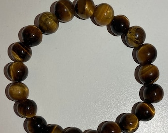 May include: A brown and gold tiger's eye beaded bracelet. The bracelet is made of round beads and has a simple design.