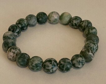 May include: A green and white speckled stone bead bracelet. The bracelet is made of round beads that are strung together on a clear elastic cord.