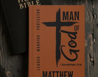 May include: A brown leather-bound book with the words "MAN OF God" and a black cross design. The name "Matthew" is printed at the bottom. The book is next to a black book that says "HOLY BIBLE".
