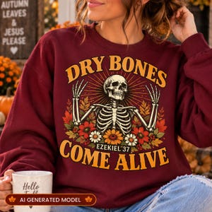 May include: A maroon crewneck sweatshirt featuring a graphic print of a skeleton with raised arms surrounded by autumn leaves and flowers. The text reads DRY BONES COME ALIVE and EZEKIEL 37 in yellow and orange lettering against a dark background.
