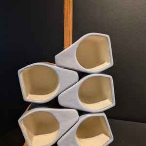 May include: A set of six light blue ceramic mugs with a wooden stand. The mugs are stacked in a staggered pattern, with the top mug facing forward. The stand is made of wood and has a rectangular shape.